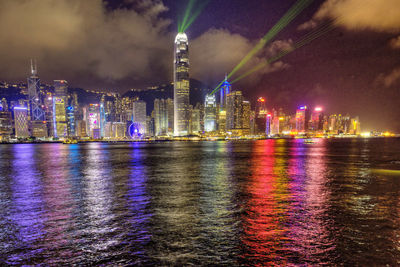 Illuminated buildings by river against sky at night