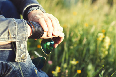 Midsection of man holding sunglasses sitting outdoors