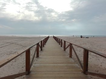 Empty jetty leading to sea against cloudy sky