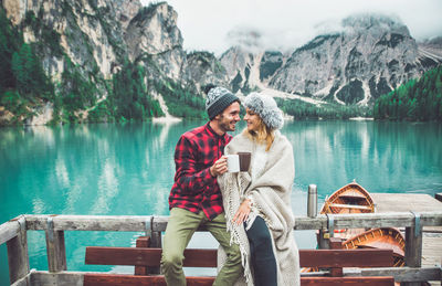 Couple sitting on mountain by lake against mountains