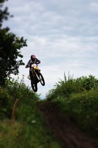 Low angle view of motocross racer performing stunt over dirt road against sky