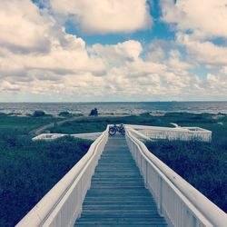 Footpath leading towards sea against cloudy sky