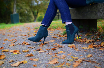 Low section of woman sitting on bench by autumn leaves on street