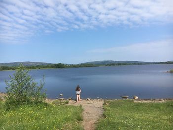 Rear view of girl walking at lakeshore against sky