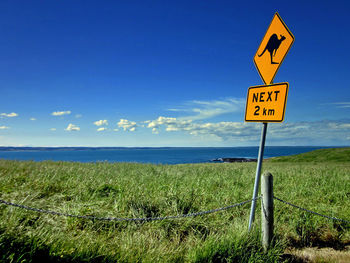 Information sign on grass by sea against blue sky