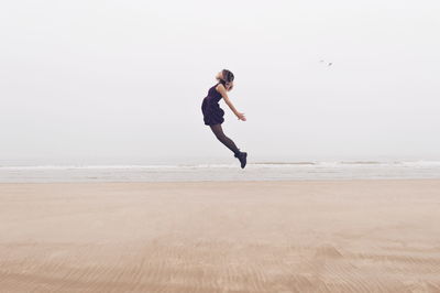 Full length of woman jumping at beach against sky