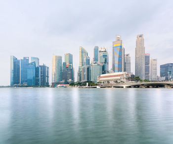 Sea by modern buildings in city against sky