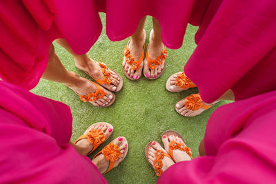 Low section of female friends wearing pink dress and floral flip-flop while standing on field