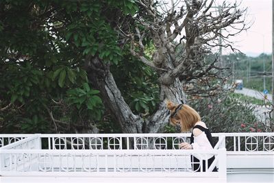 Portrait of woman by railing against trees