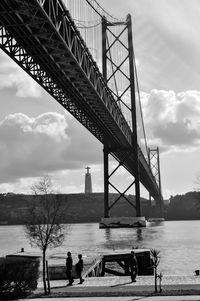 Low angle view of april 25th bridge over river against cloudy sky