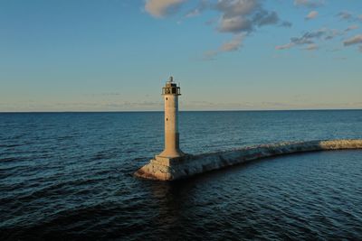 Lighthouse by sea against sky during sunset