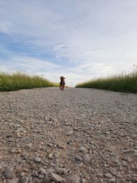 Man cycling on road amidst field against sky