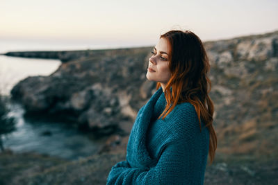 Young woman looking away while standing on rock against sea