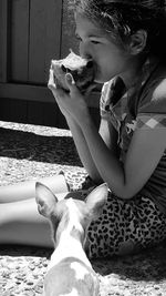 Girl eating fruit while sitting by puppy