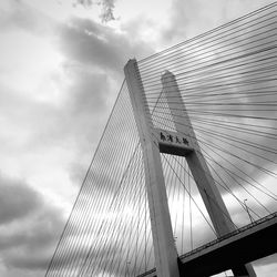 Low angle view of suspension bridge against cloudy sky