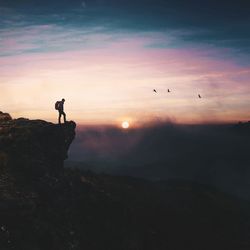 Side view of man standing on cliff against cloudy sky during sunset