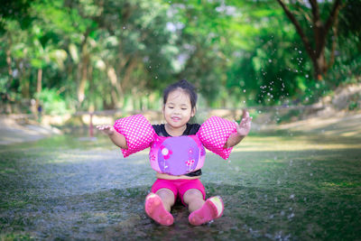 Happy girl splashing water while sitting on wet land