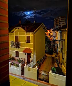 Illuminated street amidst buildings against sky at night