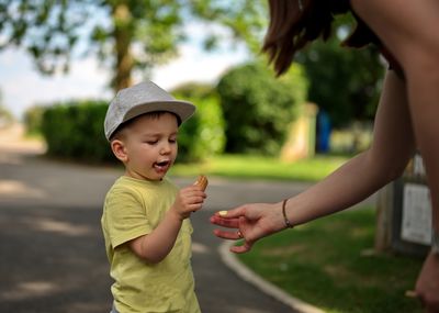 Portrait of little toddler in a park eating ice cream with a help of his mother