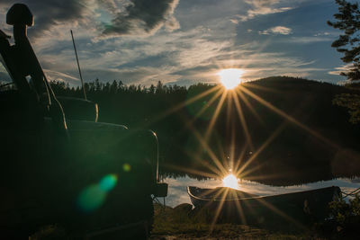 Car parked by lake against sky during sunset