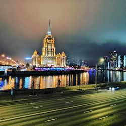 Illuminated building reflecting on river against sky at night