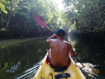 Rear view of man holding boat against river