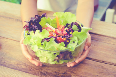 Cropped hands of person holding salad in bowl on wooden table