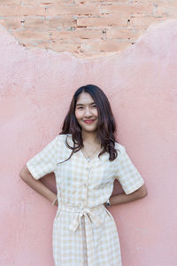 Portrait of smiling young woman standing against wall outdoors