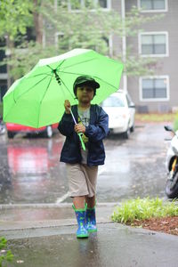 Boy walking with green umbrella on street during monsoon