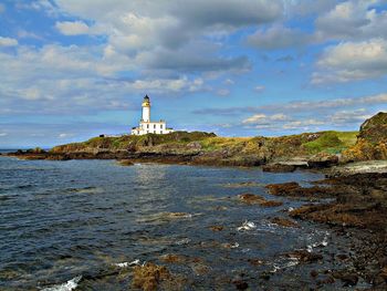 Lighthouse amidst sea and buildings against the sky