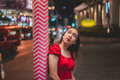 Portrait of woman standing by illuminated street in city at night