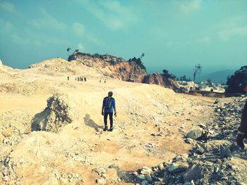 Rear view of man walking on rock against sky