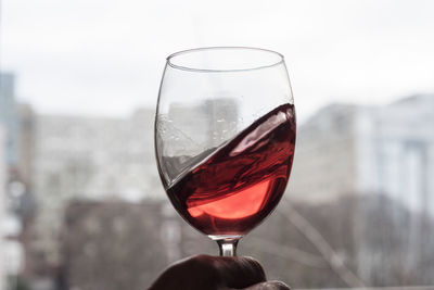 Cropped hand of man swirling wineglass against window