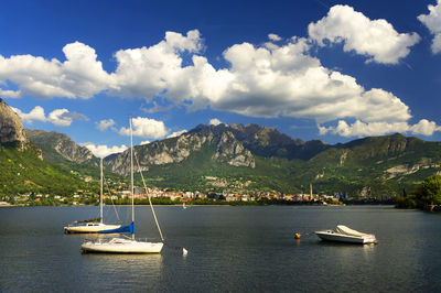 Boats at lake como by mountains against cloudy sky