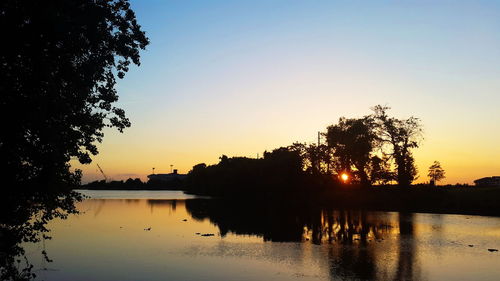 Silhouette trees by lake against clear sky during sunset