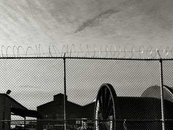 Cranes against sky seen through chainlink fence