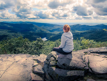 Rear view of woman sitting on rock against sky