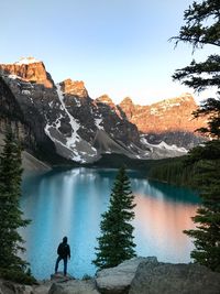 Man standing on rock by lake against clear sky