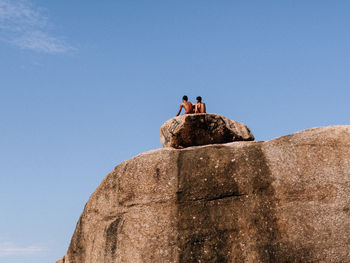 Low angle view of man standing on rock against clear blue sky