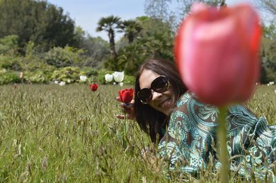 Portrait of woman in sunglasses with red flowers on field
