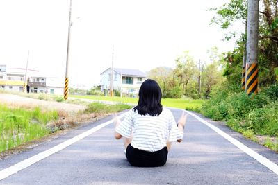 Rear view of man sitting on road against clear sky