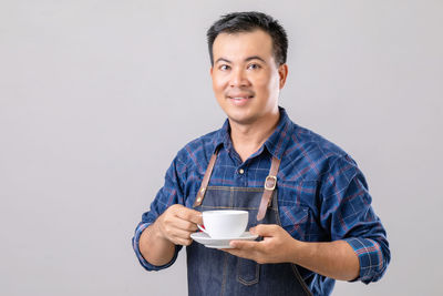 Portrait of young woman drinking coffee while standing against white background