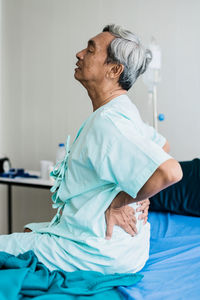 Side view of man sitting on bed