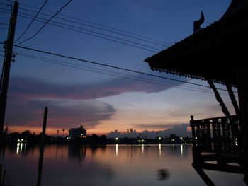 Silhouette buildings by river against sky during sunset