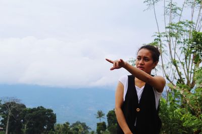 Young woman standing by plants against sky