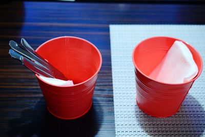 High angle view of silverware and tissue papers in red disposable glass on table