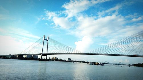 Suspension bridge over river against cloudy sky