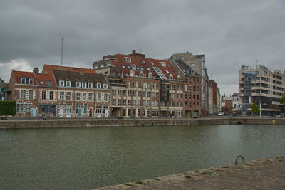 View of buildings by river against cloudy sky