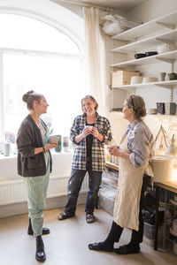 Happy female colleagues standing with coffee cups while talking at ceramics store