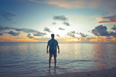 Rear view of man standing at beach during sunset